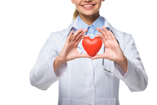 Beyaz önlük beyaz izole kırmızı kalp tutan genç doktor kırpılmış görünümünü - Fotoğraf, Görsel