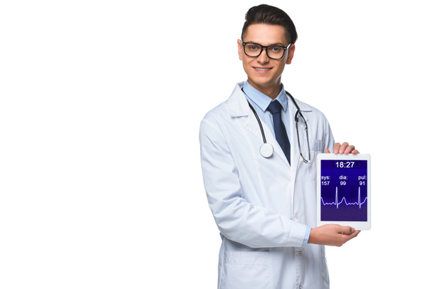 glücklicher junger Arzt hält Tablette mit Pulsmesser auf dem Bildschirm isoliert auf weiß - Foto, Bild