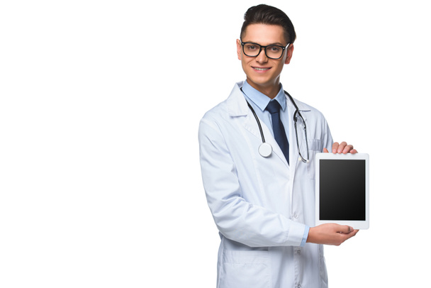 smiling young doctor holding tablet with blank screen isolated on white - Photo, image