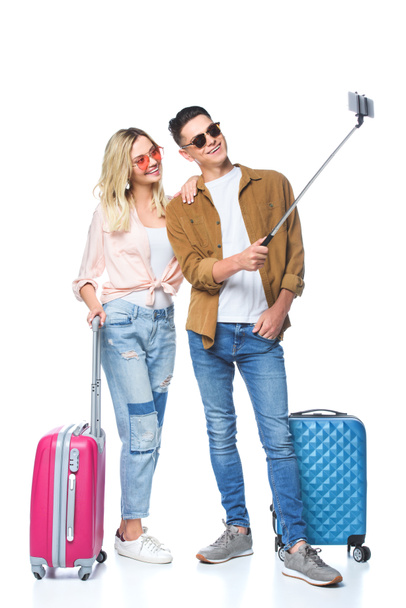 jeune couple avec valises prenant selfie avec smartphone de monopode isolé sur blanc
 - Photo, image