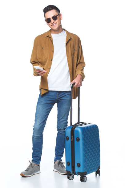 счастливый молодой человек с багажом и смартфоном изолированы на белом
 - Фото, изображение