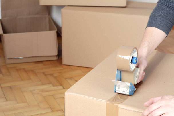 Man sealing a shipping cardboard box with tape dispenser. Indoors - Φωτογραφία, εικόνα