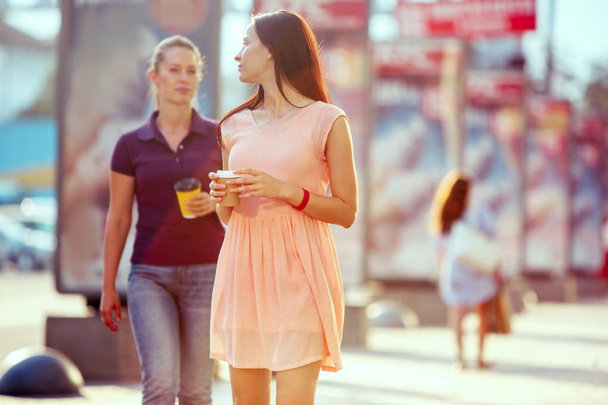Beautiful girls holding paper coffee cup and enjoying the walk in the city - Фото, зображення