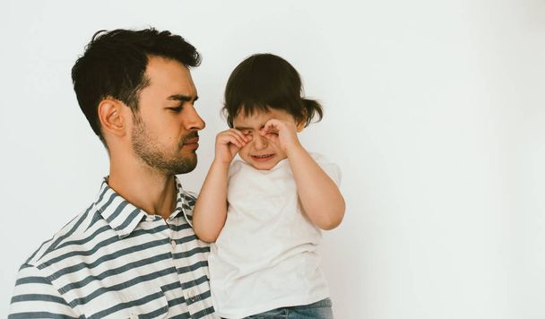 Portrait of handsome hipster father holding his crying daughter. Young dad embrace his sad child. Attractive man support his little toddler girl. Childhood and fatherhood. Lifestyle family. - Foto, Imagen