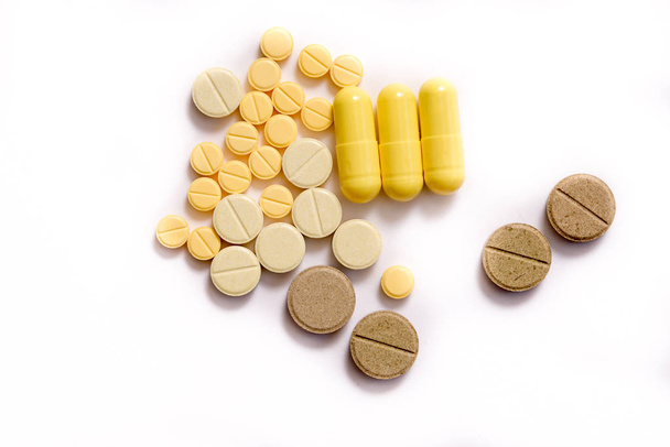 different yellow brown beige herbal orange pills and gelatin capsules on an isolated white background - Foto, Imagen