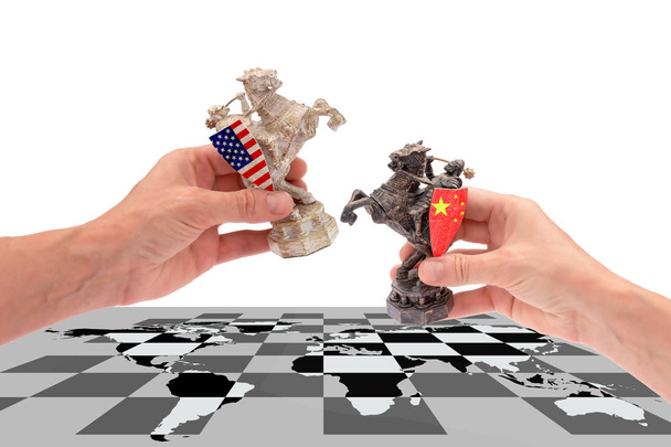 Guerra comercial entre Estados Unidos y China. manos sostienen dos piezas de ajedrez de un caballo, con banderas americanas y chinas colocándolas en un tablero de ajedrez con un mapa del mundo, aisladas sobre un fondo blanco con espacio para copiar
. - Foto, imagen