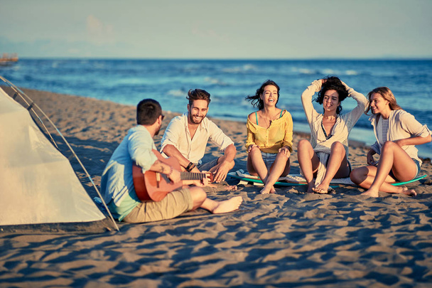 Group of happy friends relaxing with playing guitar and sing a song on sea beach - Zdjęcie, obraz
