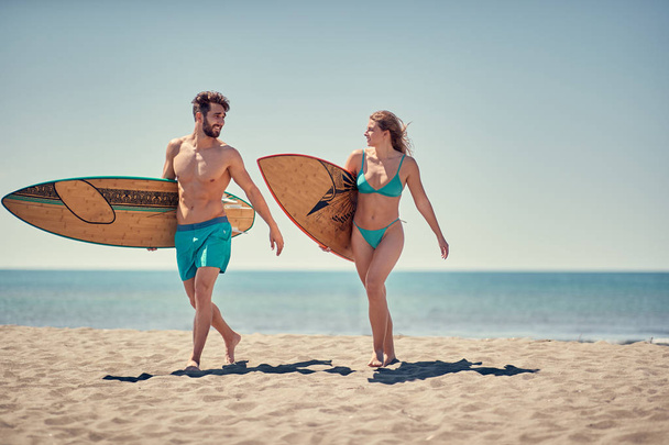 Healthy Active Lifestyle. Surfing. Young man and woman surfers going together to surf at the beach  - 写真・画像