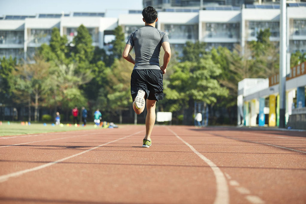 joven asiático hombre macho atleta funcionamiento entrenamiento ejercicio en pista, vista trasera
. - Foto, Imagen