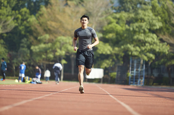 fiatal ázsiai férfi férfi sportoló fut a képzés gyakorló pályán. - Fotó, kép