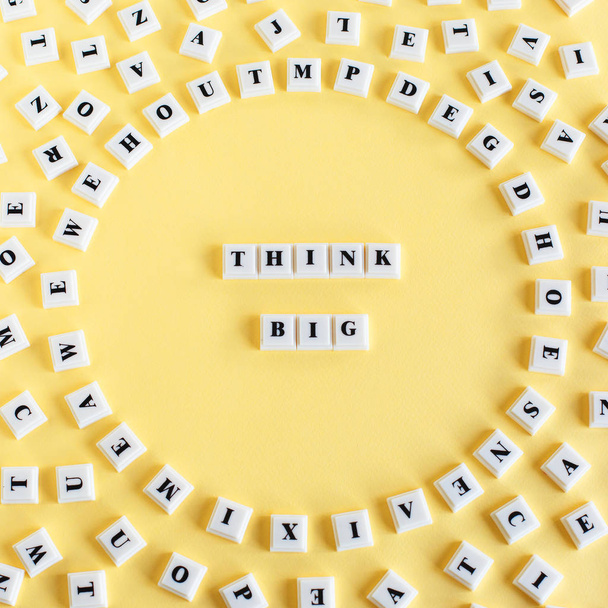 Blocco di plastica cubo con la parola PENSARE GRANDE e intorno sparse singole lettere su sfondo giallo
. - Foto, immagini