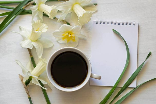 Notepad, cup of coffee and daffodils on a white background - Φωτογραφία, εικόνα