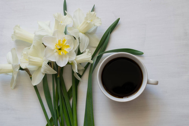 Beautiful daffodils and a cup of coffee on a white background. Cup of coffee and white flowers. - Photo, image