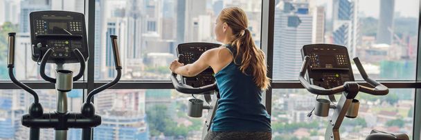 Young woman on a stationary bike in a gym on a big city background. - Foto, imagen