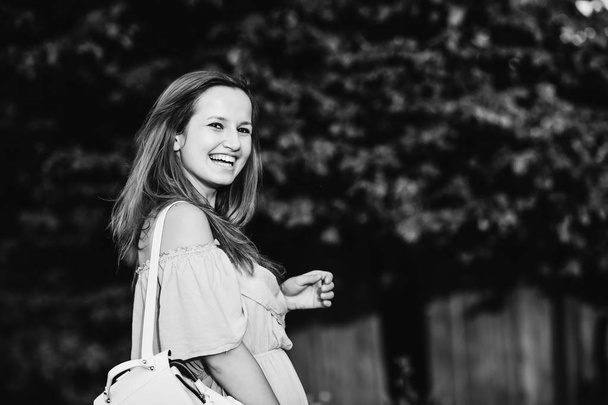sincere smile of girl and stylish dress and backpack on shoulder on black and white photography - Photo, Image