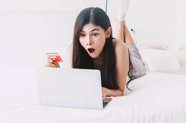 Mujer de compras en línea con cuaderno y tarjeta de crédito en la cama en casa
 - Foto, imagen