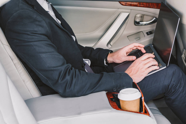 Przystojny biznesmen działa na laptopie siedząc na tylnym siedzeniu samochodu - Zdjęcie, obraz