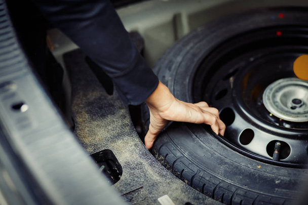 Close up mechanic hand taking spare tire at boot - Photo, image