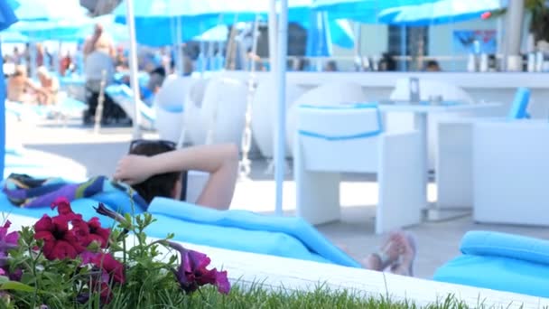 Een vrouw in een luxeresort, ontspant op de ligstoelen bij het zwembad in de buurt van de bloemen. Begrip: reizen, vakantie, ontspanning, hotel. - Video