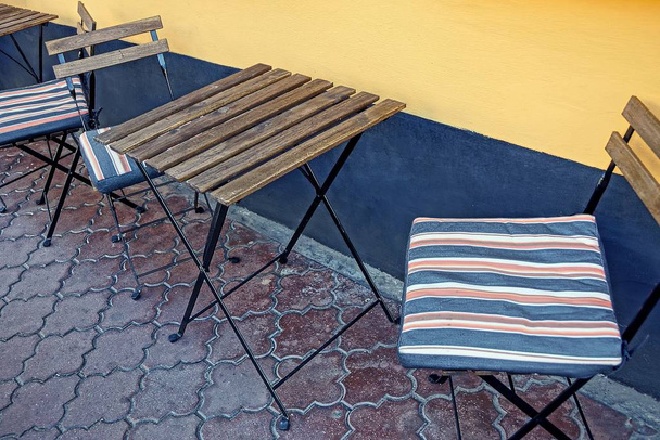 деревянный стол и полосатые стулья на тротуаре возле стены на улице
 - Фото, изображение