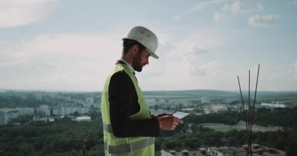 Young businessman stand up on the top of construction site analyzing uses a tablet the building construction - Felvétel, videó