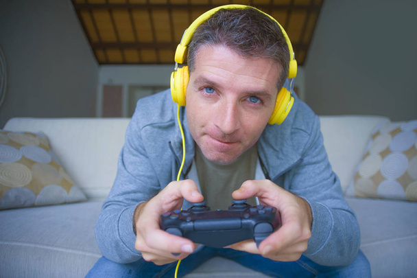 lifestyle portrait of young happy and excited gamer man with headphones  playing video game at home having fun on sofa couch holding controller concentrated in gaming concept  - Foto, immagini