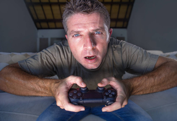 lifestyle portrait of young stressed and excited gamer man playing video game at home living room having fun on sofa couch holding controller concentrated and stressed in gaming emotion concept - Foto, Bild