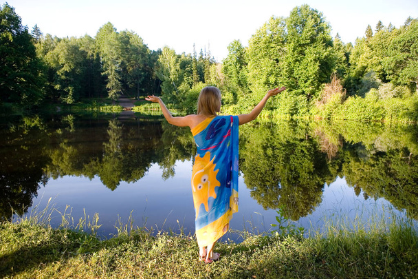 A young blonde woman stands with her back to the camera and raised her hands in different directions. Man in nature in the morning. - Foto, Bild