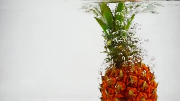 De rijpe ananas valt in het water in slow motion. Vruchten op geïsoleerde witte achtergrond. - Video