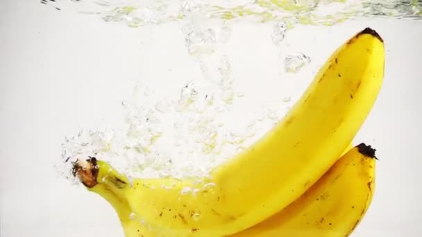 Die Bananen fallen mit vielen kleinen Blasen ins Wasser. Video von Bananen auf isoliertem weißen Hintergrund. - Filmmaterial, Video