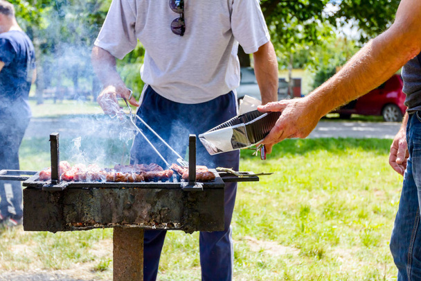 L'homme sort des kebabs rôtis avec des pinces en métal, les retire du barbecue dans un pot en plastique
.  - Photo, image