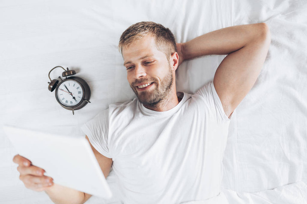 Handsome man using a digital tablet in bed at home - Foto, afbeelding