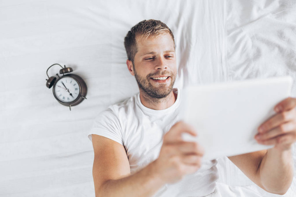 Handsome man using a digital tablet in bed at home - Foto, Imagen