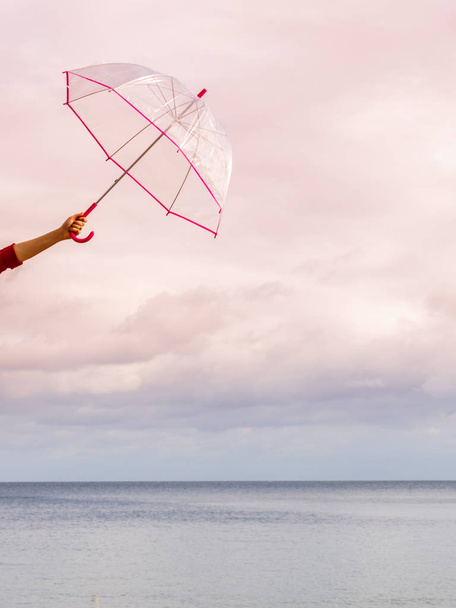 Unerkennbare menschliche Hand, die einen durchsichtigen Regenschirm gegen den wolkenverhangenen Himmel hält. Meteorologie, Objektkonzept zur Wettervorhersage. - Foto, Bild