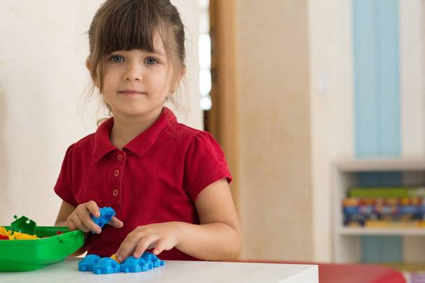 Niña jugando juguetes en casa o en la guardería. Los niños preescolares construyen flores con bloques de plástico. Niño pequeño en la guardería
. - Foto, imagen