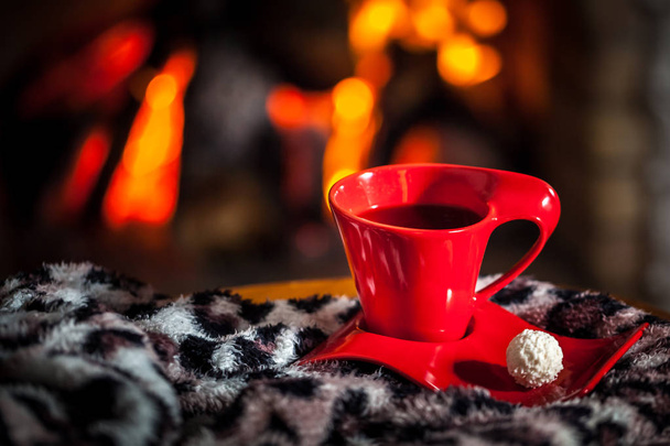 Red cup of tea or coffee and chocolate near fireplace on the table. Winter and Christmas holiday concept. - Photo, Image