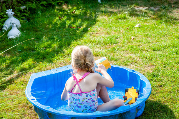 Little girl enjoying a hot summer day while usin her sandpit as swimming pool - Fotoğraf, Görsel