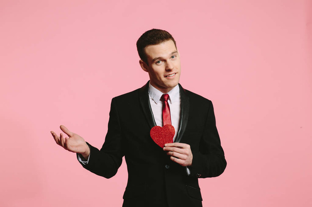 Sevgililer günü için kırmızı bir kalp tutan siyah elbiseli yakışıklı adam - Fotoğraf, Görsel