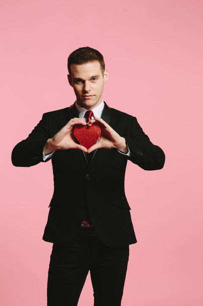Handsome man in a black suit holding a red heart for Valentine's Day - Foto, imagen