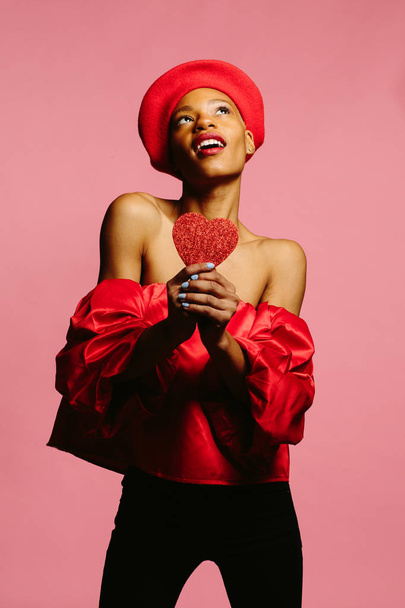 ελκυστική νεαρή γυναίκα με κόκκινο χρώμα, χαμογελώντας και κρατώντας μια κόκκινη καρδιά, Γίνε ο Βαλεντίνος μου  - Φωτογραφία, εικόνα