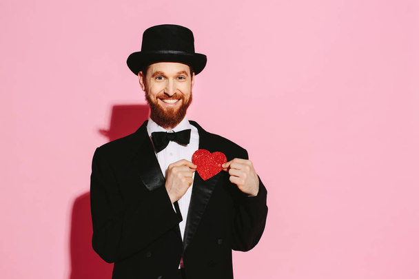 Bir smokin ve silindir şapka kırmızı bir kalp tutan gülümseyen adam - Fotoğraf, Görsel