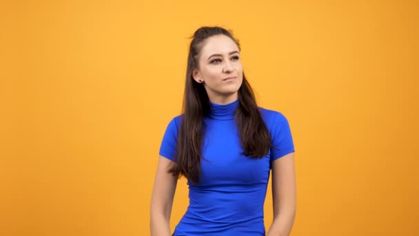 Krásná žena v modrém tričku nudu na zářivé oranžové pozadí ve studiu - Záběry, video
