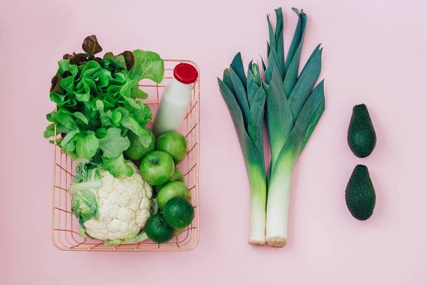Korb mit grünem Obst und Gemüse auf pastellrosa Hintergrund - Foto, Bild