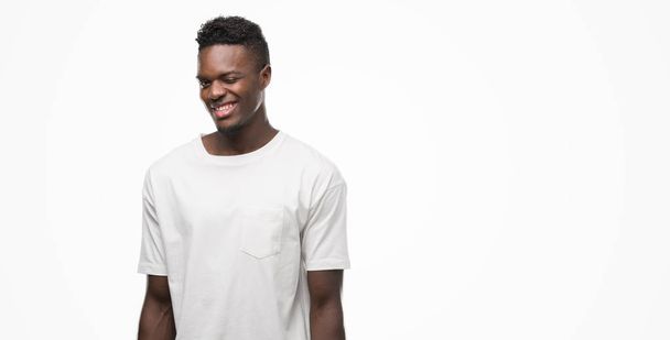 Afro-amerikai fiatalember visel, fehér póló Kacsintó szexi kifejezés, vidám és boldog arc néz a kamerába. - Fotó, kép