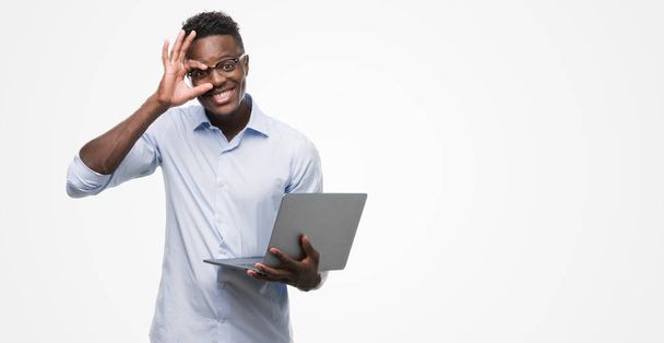 Mladý americký podnikatel pomocí přenosného počítače s šťastný obličej s úsměvem dělá ok znamení rukou na oko dívá skrze prsty - Fotografie, Obrázek