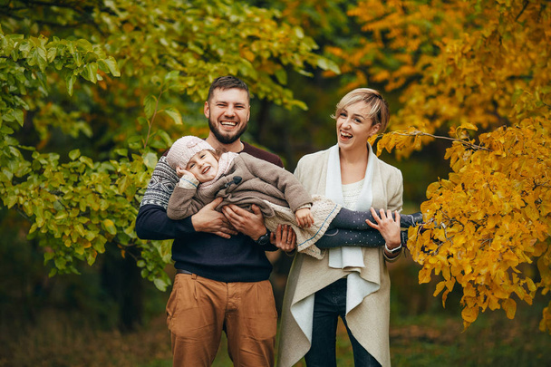 Les parents heureux s'amusent, rient et lèvent leur fille sur leurs mains pendant la promenade dans la forêt d'automne
. - Photo, image