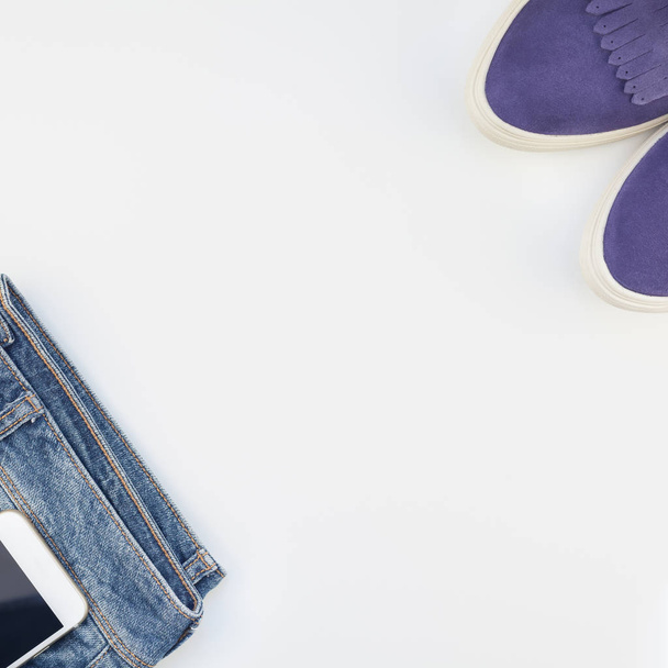 Kwadrat z płaskim położyć zamszowe buty, niebieskie jeansy i smartphoneon białe tło z miejsca kopii. Ogólny widok dama dorywczo strój. Hipster modny wygląd widok z góry - Zdjęcie, obraz