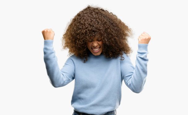 Gülümseyen ve başarı için çığlık çok mutlu ve heyecanlı kaldırdı, silah ile kazanan jest yapıyor bir kazak giyen Afrikalı-Amerikalı kadın. Kutlama kavramı. - Fotoğraf, Görsel