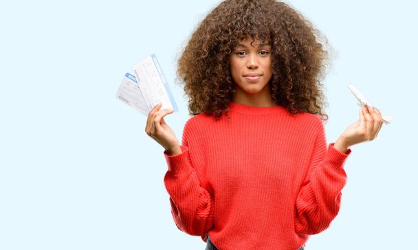 Femme afro-américaine tenant des billets d'avion carte d'embarquement avec une expression confiante sur le visage intelligent pensée grave
 - Photo, image