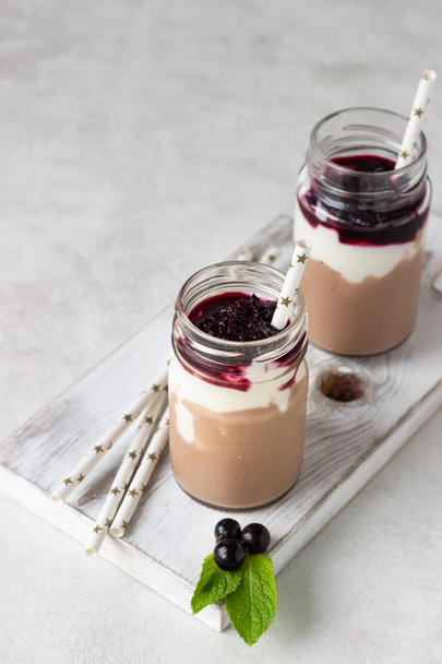 Two bottles of chocolate and banana smoothie with natural yoghurt and black currant. Delicious and healthy breakfast concept. Selective focus. Copy space. - Фото, изображение